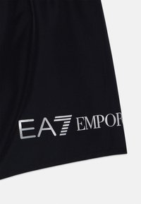 Fekete sportnadrág fényes ezüst "EA7 EMPORIO" logóval az alján. Sima textúra klasszikus dizájnnal.