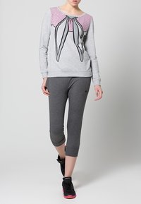 Sudadera gris con frente de lunares rosas y diseño gráfico de lazo, combinada con pantalones capri grises ajustados y zapatillas deportivas negras.