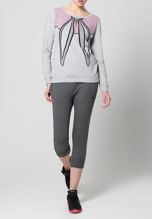 Gray sweatshirt with pink polka dot front and graphic bow design, paired with fitted gray capri pants and black athletic shoes.