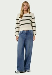 White striped knit sweater with black stripes, paired with wide-leg blue denim jeans. Soft texture and relaxed fit visible.