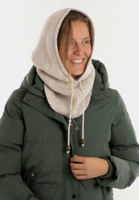 Beige gebreide capuchonsjaal met een geribbelde textuur, gecombineerd met een groene pufferjack, voorzien van een rits en toggles voor sluiting.