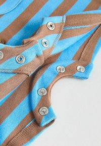 Gros plan sur un tissu rayé marron et bleu avec des boutons-pression métalliques partiellement ouverts sur un vêtement.