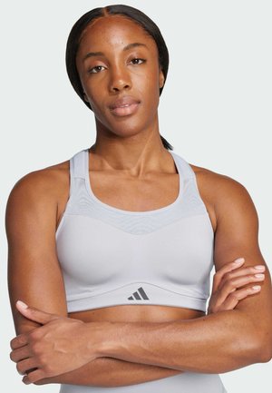 Light gray athletic sports bra made of fitted fabric, featuring a curved neckline, wide straps, and a subtle logo accent at the bottom.