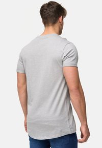 T-shirt gris à manches courtes avec un col rond, offrant une coupe décontractée et un dos plus long. Fabriqué en tissu doux avec une texture subtile.