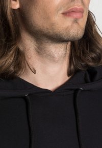 Black hooded sweatshirt with a simple design, featuring a textured fabric and drawstring, partially covering the neck area.
