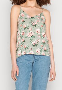 Haut sans manches floral en vert clair, orné de roses roses et de feuilles vertes. Tissu doux avec un décolleté en V, coupe ample et ourlet légèrement arrondi.