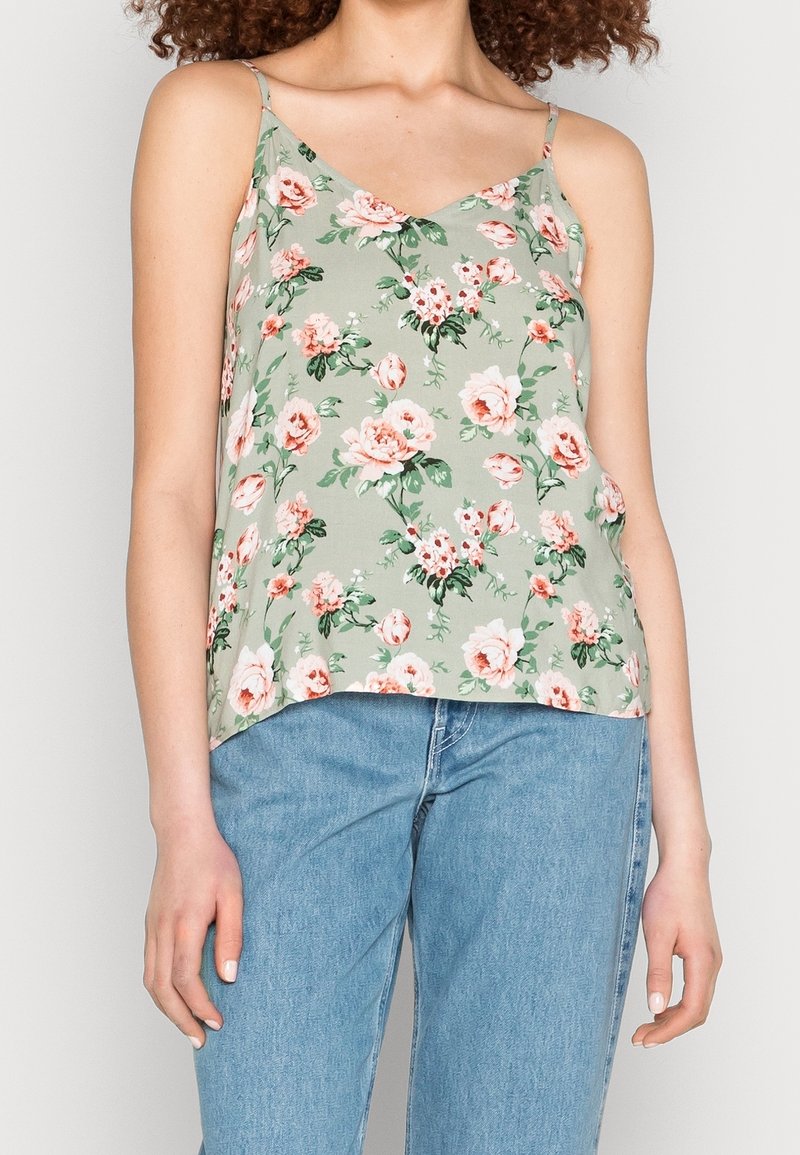 Haut sans manches floral en vert clair, orné de roses roses et de feuilles vertes. Tissu doux avec un décolleté en V, coupe ample et ourlet légèrement arrondi.