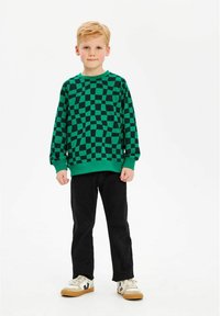 Grön rutig sweatshirts med ribbad rundhals och muddar, kombinerad med svarta byxor och vita sneakers med bruna sulor.