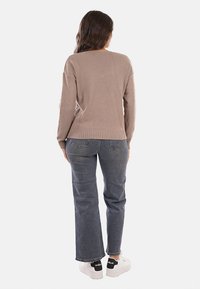 Pull beige dalla vestibilità relaxed, bordi a coste e polsini, abbinato a jeans grigio scuro e sneakers bianche. Texture liscia, design semplice.