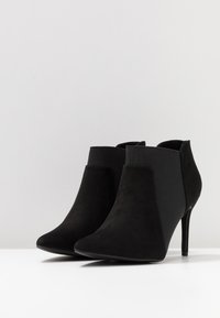Schwarze Ankle Boots mit einem Wildleder-Obermaterial, spitzer Zehenpartie und Stiletto-Absatz. Das Design umfasst elastische Einsätze an den Seiten.