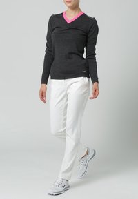 Pull à manches longues gris foncé avec un col en V rose, associé à un pantalon blanc et des chaussures de sport grises. Design simple et ajusté.