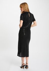 Vestito nero con paillettes, maniche corte e dettaglio a oblò sul retro, dotato di gonna fino al ginocchio e silhouette fluida e aderente.