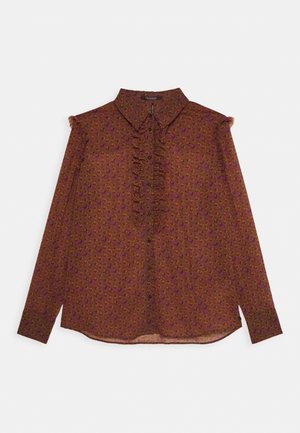 Blouse marron à manches longues avec un motif floral en violet et rose. Présente un devant froncé, un col pointu et une fermeture à boutons. Texture de tissu douce.