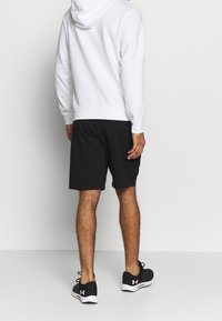 Sweat à capuche blanc avec poignets, associé à un short de sport noir. Des baskets noires complètent la tenue. Design minimaliste sans motifs.
