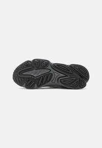 Black athletic shoe sole with textured rubber, featuring various contoured patterns and grooves for traction and support.