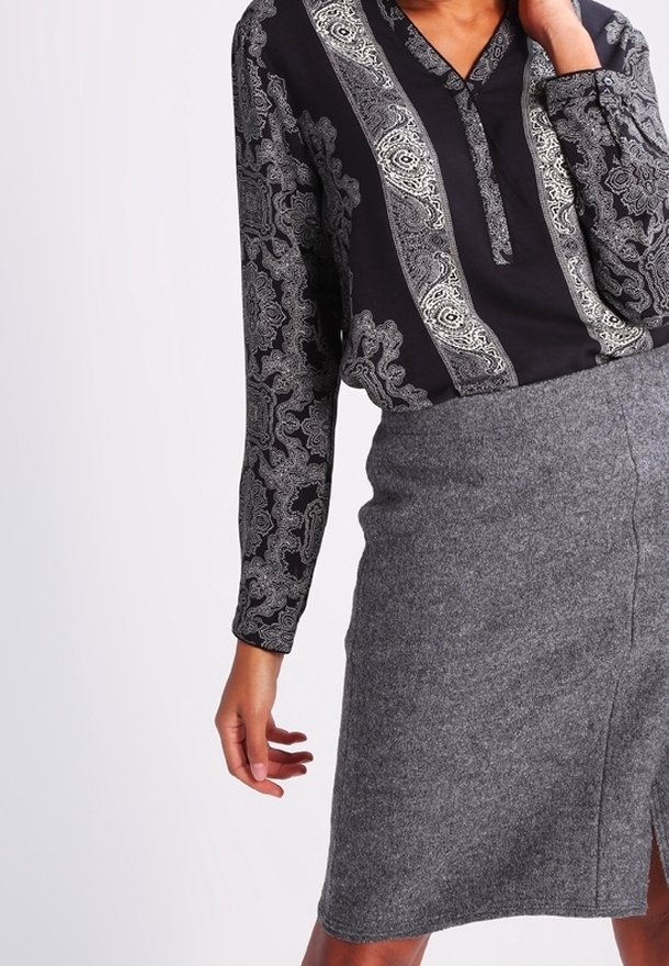 Blouse à manches longues en tissu noir avec des motifs paisley blancs complexes, associée à une jupe crayon en laine grise avec une fente frontale.