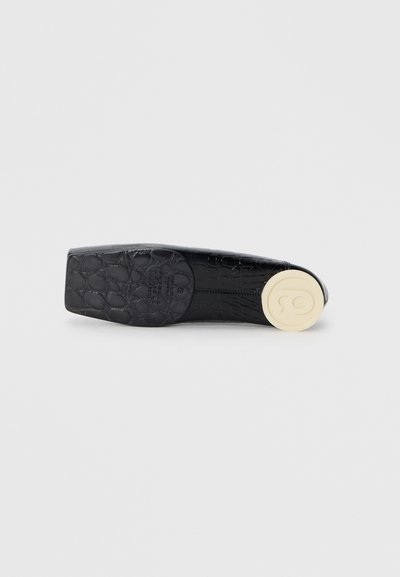 Svart lackskinnssko med krokodilsmönster, platt design, fyrkantig tå och en rund beige sula med logodetalj.