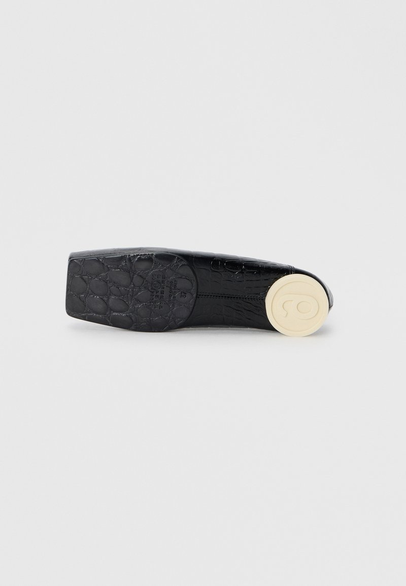 Black patent leather shoe with a crocodile texture, flat design, square toe, and a round beige sole with a logo detail.