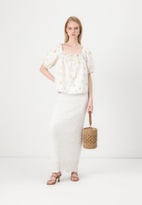 Biała bluzka w kwiatowy wzór z puff sleeves, zestawiona z fakturowaną białą maksiówką. Dodatki to brązowe sandały na obcasie i pleciona torebka.