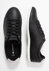 Baskets montantes synthétiques noires avec un embout arrondi, une tige texturée, une semelle en caoutchouc blanche et un accent doré sur le côté. Logo de la marque visible à l'intérieur.