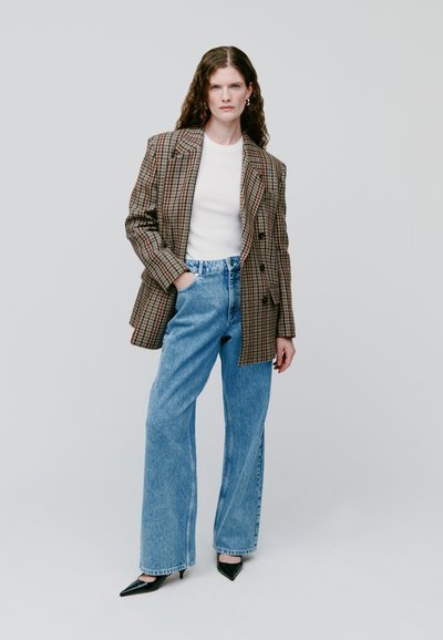 Blazer extragrande a cuadros en marrón y negro, combinado con jeans de pierna ancha en azul claro. Zapatos de tacón negro de punta afilada completan el look.