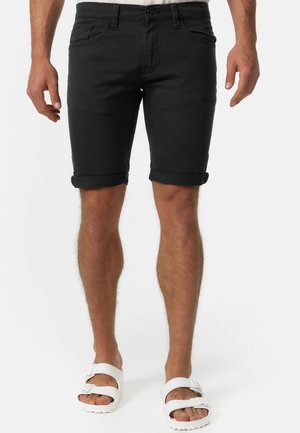 Schwarze Jeansshorts mit umgeschlagenen Säumen, Fronttaschen und einem eleganten Design. Kombiniert mit weißen Sandalen, die einen lässigen, entspannten Look zeigen.