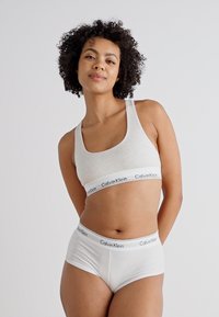Grå bomull bralette med en hvit Calvin Klein-bånd, kombinert med hvite bomullsbriefs som har et matchende logo-bånd. Glatt tekstur.