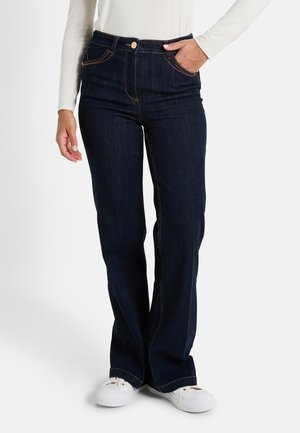 Jean en denim foncé à taille haute, avec une coupe droite, comportant des coutures contrastées discrètes et des poches avant. Porté avec des baskets blanches.