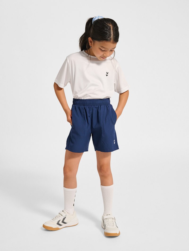 Vit t-shirt med kort ärm och en logo, tillsammans med marinblåa träningsshorts. Vita knästrumpor och ljusa sportskor fulländar outfiten.