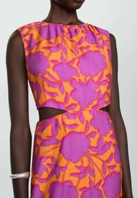 Robe orange sans manches avec motif floral violet, présentant un col froncé et des découpes triangulaires à la taille, portée avec un bracelet argenté.