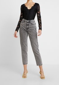 Body in pizzo nero con scollo a V, abbinato a jeans in denim grigio a vita alta. Indossato con sandali gialli con fasce. Texture lisce e contrasti.