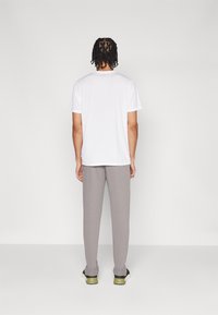Witte katoenen t-shirt met korte mouwen, gecombineerd met lichtgrijze joggingsbroek en zwarte sneakers met groene accenten, gezien vanuit de achterkant.