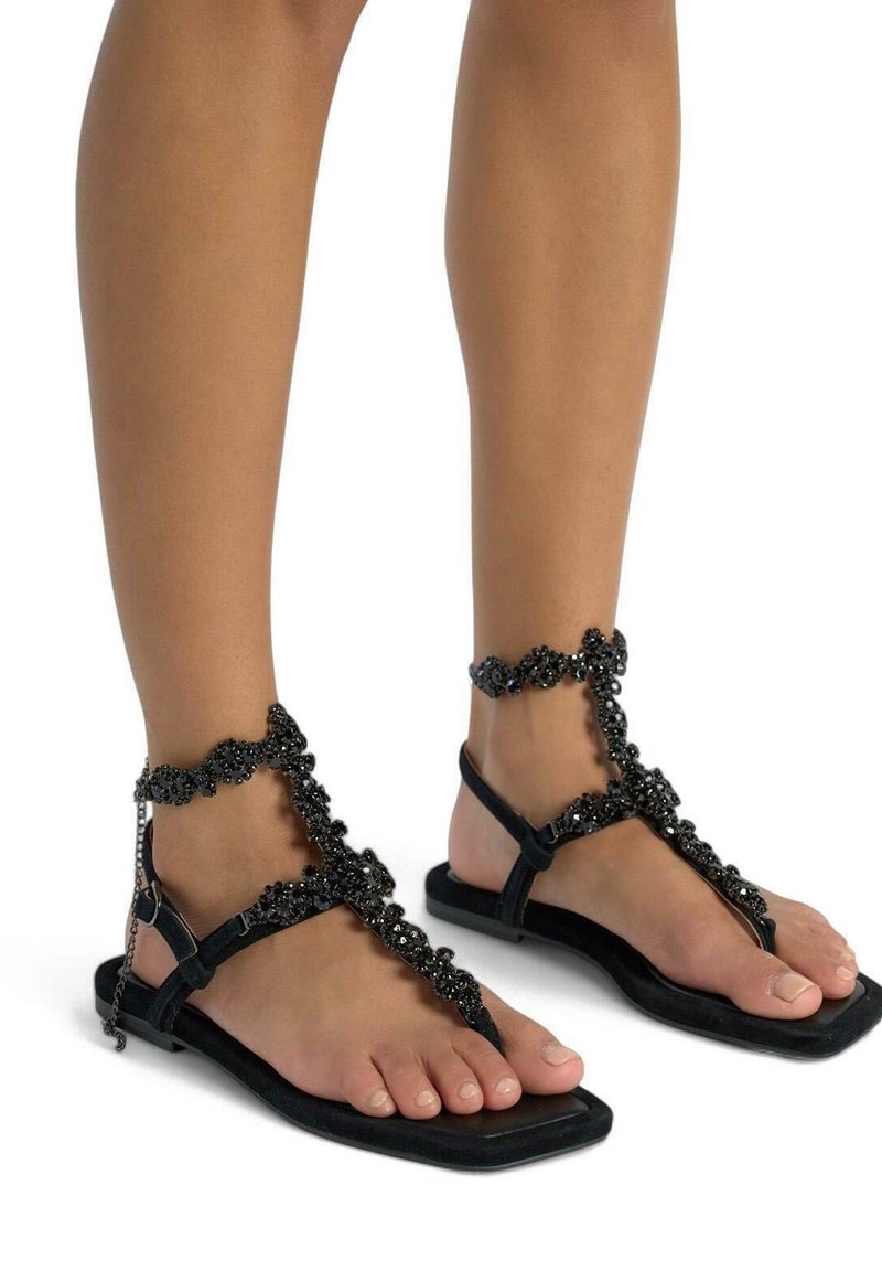 Zwarte platte sandalen met kralenaccenten, voorzien van een teenstuk en enkelband, met een benadrukte textuur en versierde ontwerpen.