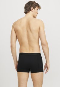 Black cotton boxer shorts with a wide elastic waistband, displayed on a bare-skinned male model from the back, featuring a fitted design.