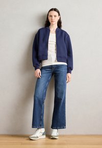 Tume navy sinine bomber-jakk, beež topp, laiad sinised teksad ja valged tossud roheliste detailidega. Lihtne disain ribistatud varrukate ja äärega.