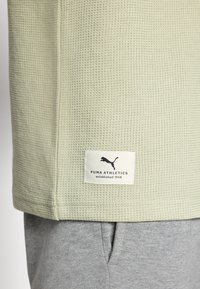 Lichtgroene, gestructureerde sporttop met een opvallend Puma Athletics-label, gecombineerd met grijze stoffen onderkleding, wat een casual stijl laat zien.
