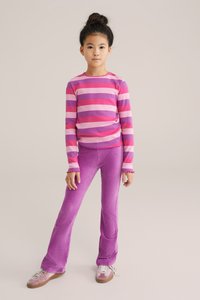 Pitkähihainen raidallinen paita vaaleanpunaisena ja vaaleanpunaisena, yhdistettynä ribattuihin violetteihin housuihin. Paidan pääntiessä on pyöreä kaula-aukko ja se on tiukasti istuva.