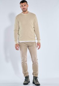 Beige Rippsweater mit Rundhalsausschnitt, kombiniert mit hellkhakifarbenen Hosen und grünen Wanderschuhen; strukturiertes Material und taillierte Passform.