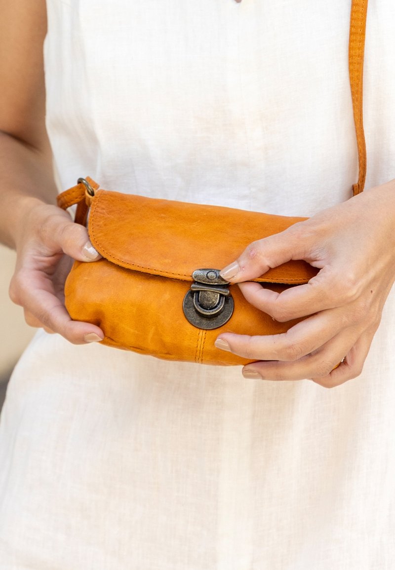 Orange clutchpung i læder med flaplukning og metalbeslag, med en lille rem til at bære. Glat tekstur, enkelt design.