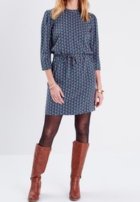 Dunkelblaues Shiftkleid mit Blumenmuster, dreiviertelärmelig und mit gebundenem Bund. Kombiniert mit knielangen braunen Lederstiefeln.
