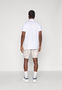 Vit polotröja, beige kortbyxor med mönster och vita sneakers. Korta ärmar och avslappnad passform. Flätat hår synligt bakifrån.