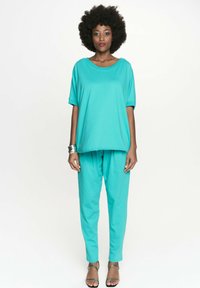 Turkusowy zestaw składający się z luźnej bluzki z krótkim rękawem oraz zwężających się spodni, wykonany z miękkiego materiału, o gładkiej teksturze i swobodnym kroju.