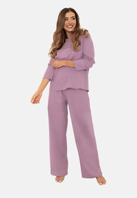 Fioletowy zestaw odzieży domowej składający się z luźnej bluzki z długim rękawem o zaokrąglonym dolnym brzegu oraz pasujących spodni w szerokim kroju, wykonany z miękkiego materiału.