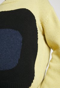 Strickpullover mit gelbem Körper, großem schwarzem und dunkelblauem abstraktem Muster, Rundhalsausschnitt und strukturiertem Stoff.