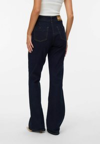 Aansluitende donkerblauwe flared jeans van denim, met achterzakken, gele stiksels en een leren merklabel op de taille.