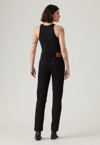 Black denim high-waisted jeans with a straight fit, featuring a tan leather patch at the back and basic pocket design.