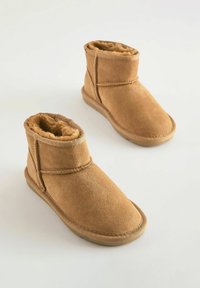 Tan suède enkellaarzen met nepbont voering, ronde neus en gestikte details. Heeft een platte rubberen zool en een eenvoudig ontwerp.