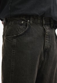 Jeans in denim scuro con taglio dritto, dotati di un design a cinque tasche, cuciture in vista e dettagli in metallo. La texture appare leggermente usurata.