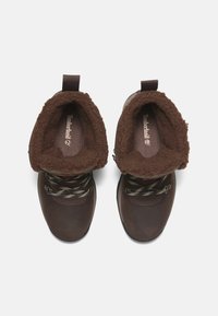 Braune Leder-Winterstiefel mit dickem Futter aus Fell, gemusterten Schnürsenkeln, metallenen Ösen und Schlaufen, von oben auf einem weißen Hintergrund betrachtet.
