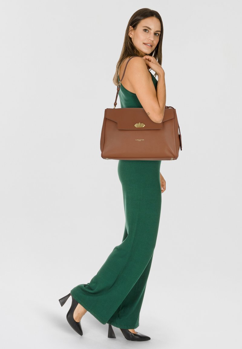 Borsa a tracolla in pelle marrone con pattina frontale e dettagli in oro, caratterizzata da una silhouette strutturata e tracolla rimovibile.